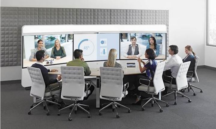 Cisco IX5000 Immersive Telepresence Suite in use. 3 screens, middle with data, 6 grey chairs close side of oval table.